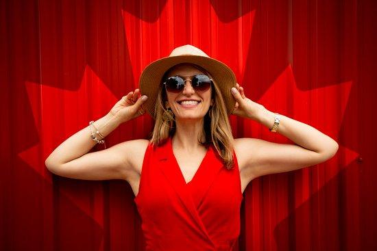 Femme au chapeau souriant devant la feuille d'érable canadienne